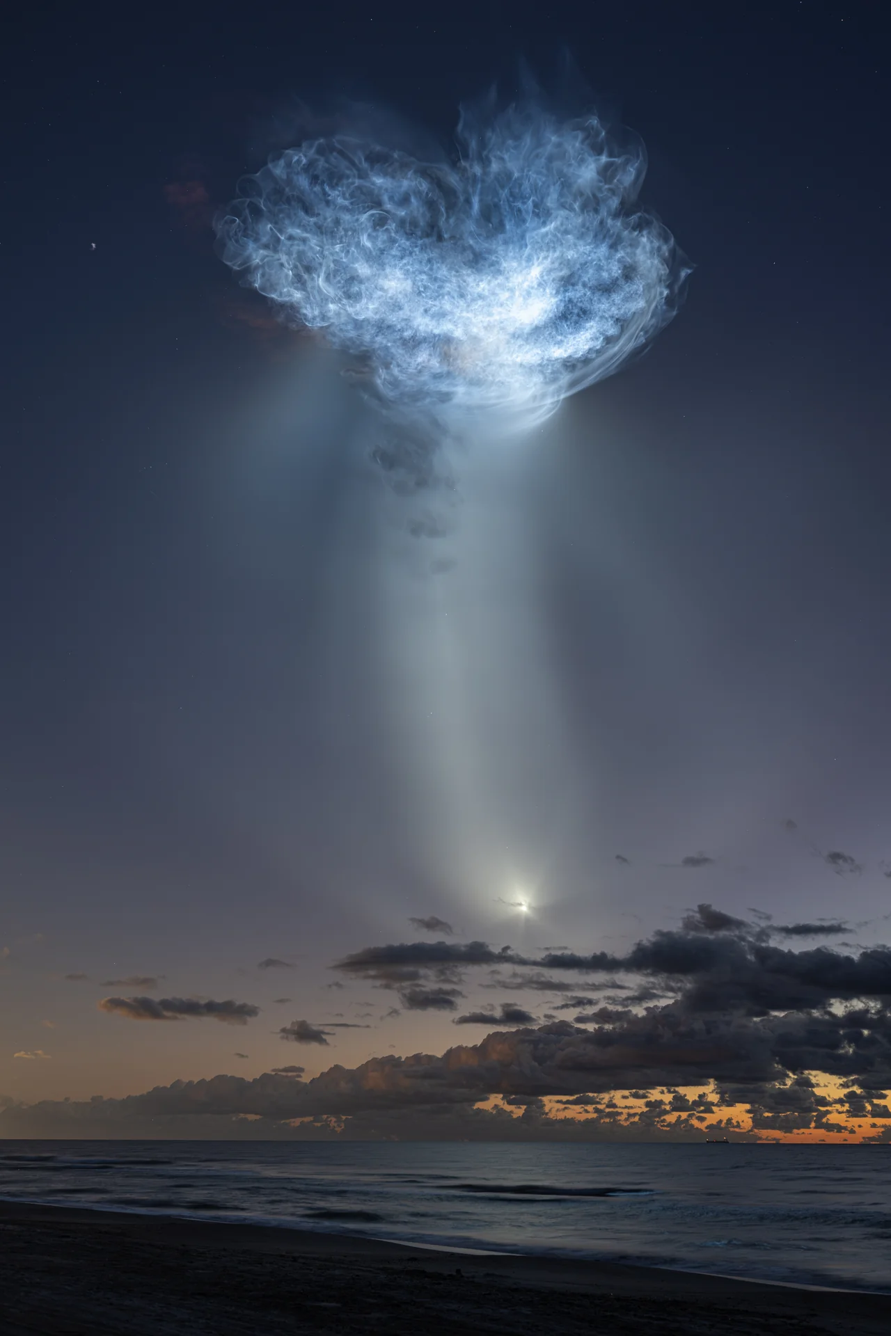 10月13日のSpaceX CRS-35打ち上げ。海と夜明け前の空の上に、太陽光を受けた排気の大きなクラゲ状の光が広がる。